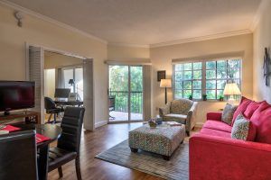 A cozy living room with modern furnishings including a sofa, armchairs, and a coffee table, featuring hardwood floors and abundant natural light from large windows.