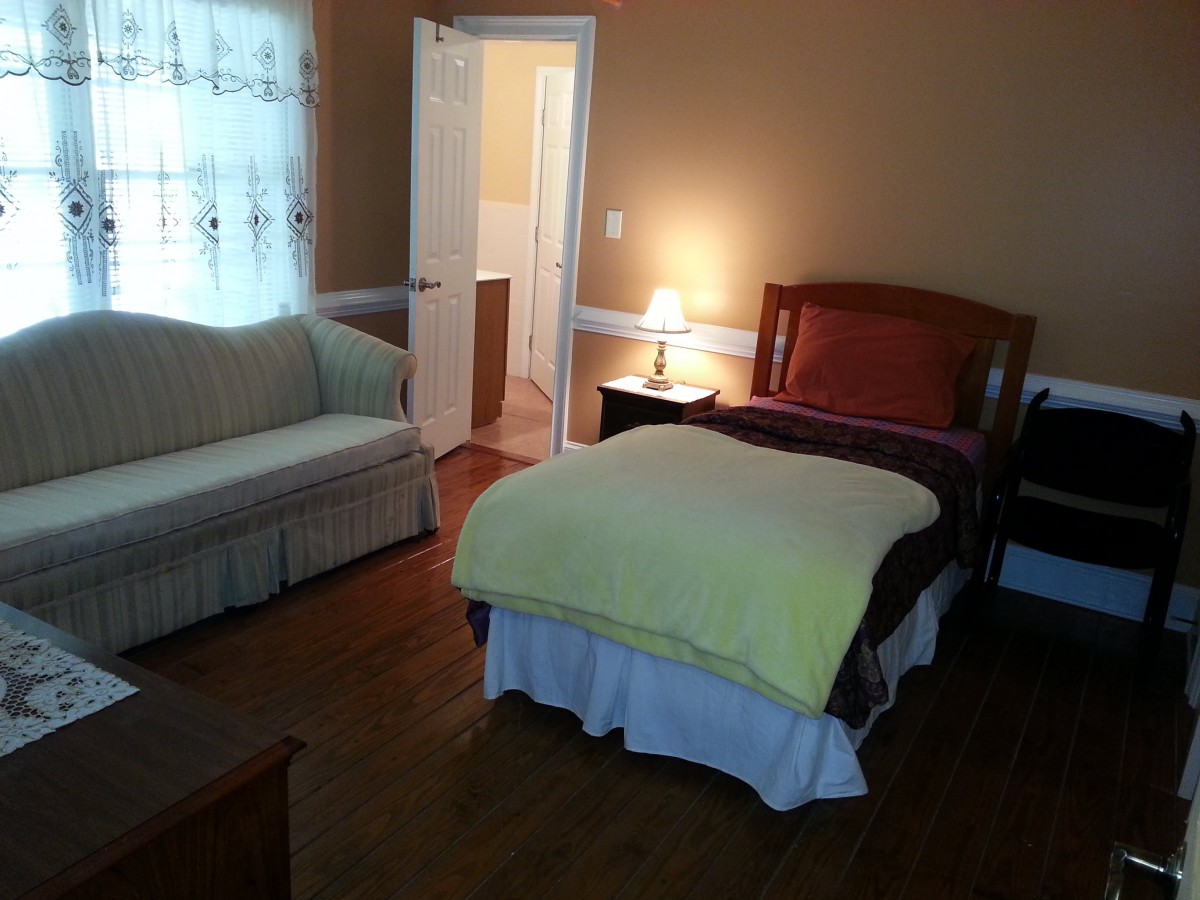 A cozy bedroom with a bed, sofa, and bedside lamp.