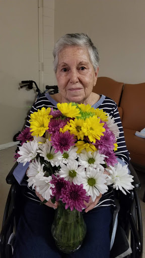 An elderly woman in a wheelchair proudly holds a beautiful bouquet of colorful flowers.
