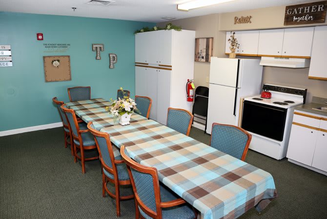 A communal dining area with a long table and seating, adjacent to a kitchen space.