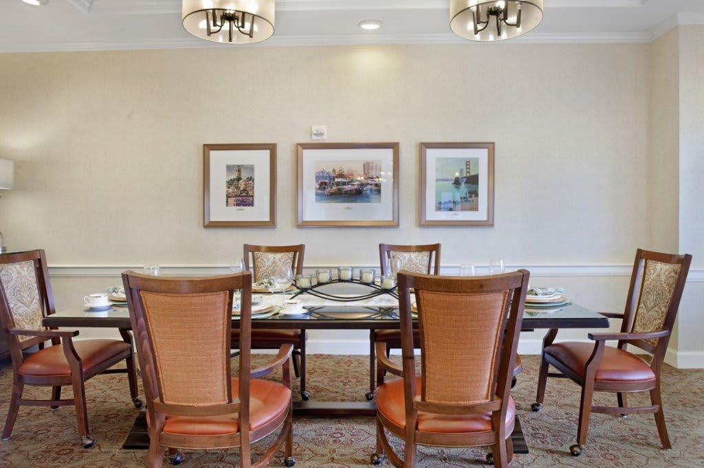 A well-decorated dining room with a wooden table, leather chairs, artwork on the wall, and elegant lighting.