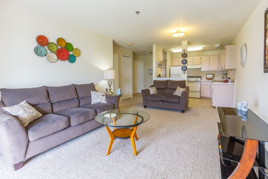 A cozy living room with comfortable sofas and a glass coffee table, adjacent to an open kitchen area.