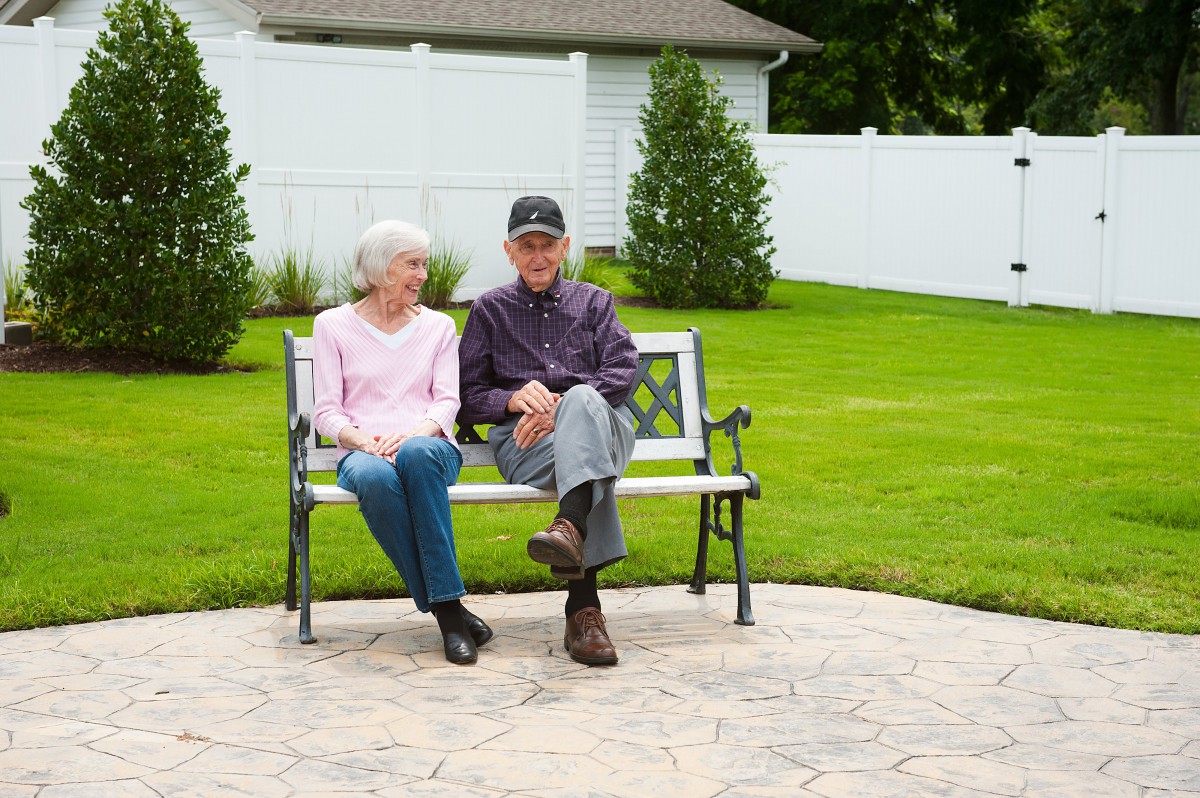An elderly couple sitting on a bench in a garden setting.