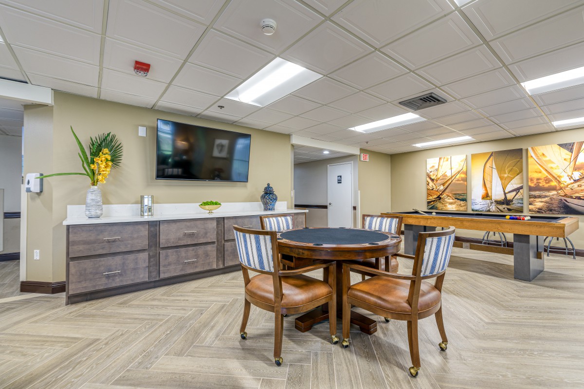 A modern room featuring a round table and chairs, with a wall-mounted television and sleek kitchenette.