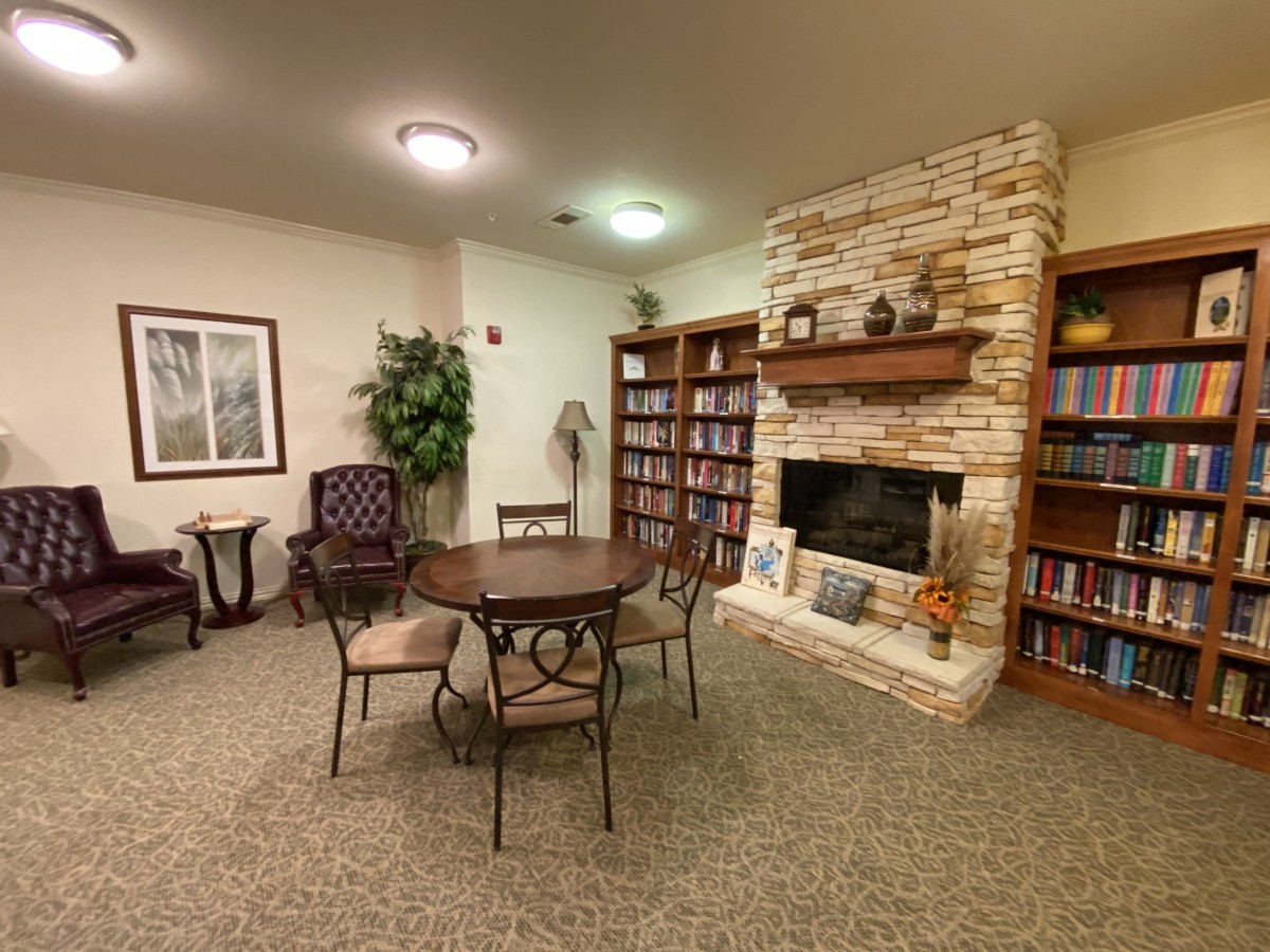 A cozy library area featuring bookshelves, a stone fireplace, and a table with chairs.