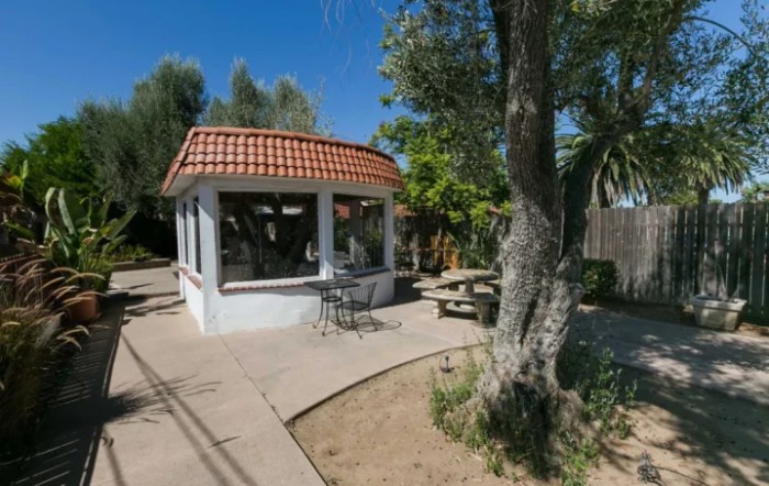 A sunny outdoor garden featuring a small gazebo, surrounded by trees and a patio area.