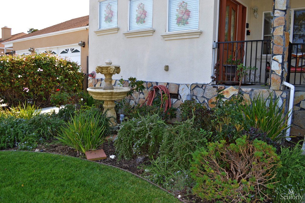 A landscaped front yard featuring a decorative fountain surrounded by various plants in front of a house.