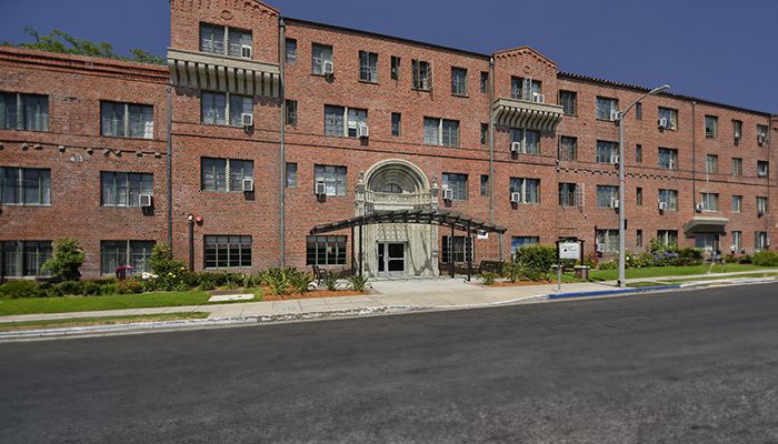 A brick apartment building with a central entrance and landscaped surroundings.