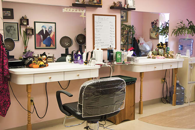 A cozy and well-decorated barbershop interior with a styling chair in front of a mirror surrounded by various beauty products.
