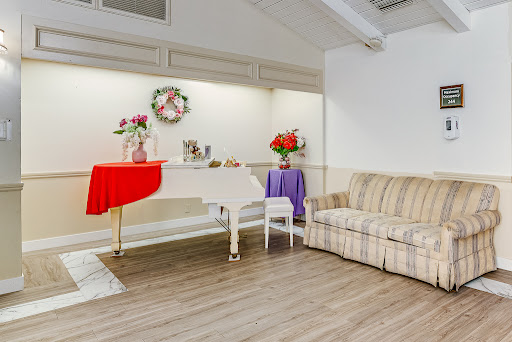 A cozy living room featuring a white piano, a striped sofa, and decorative floral arrangements on tables.