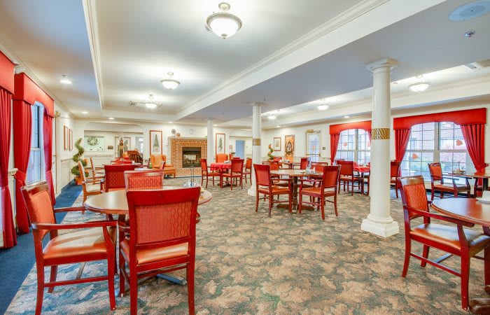 A spacious dining area featuring red chairs, tables, and elegant lighting.