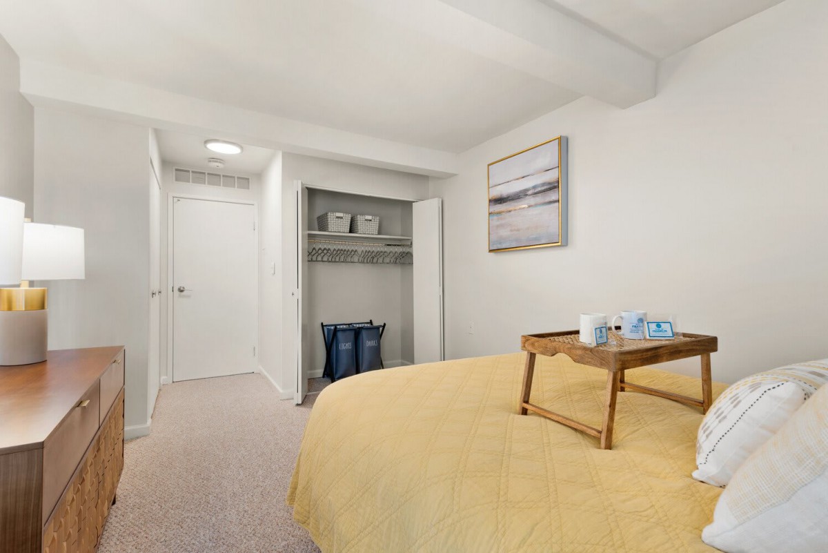 A minimalist bedroom featuring a bed with a wooden tray, an open closet, and simple decor.