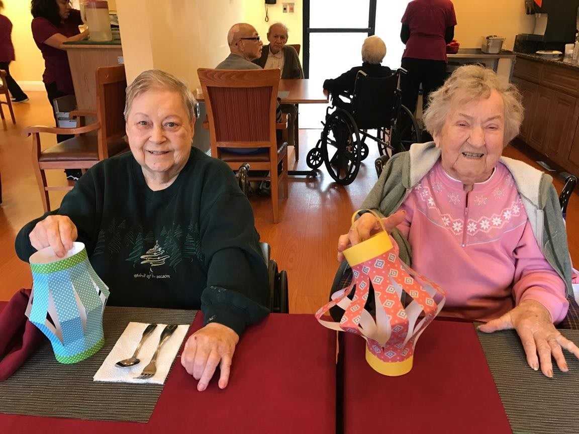 Two elderly women smiling and enjoying a meal together in a dining area.
