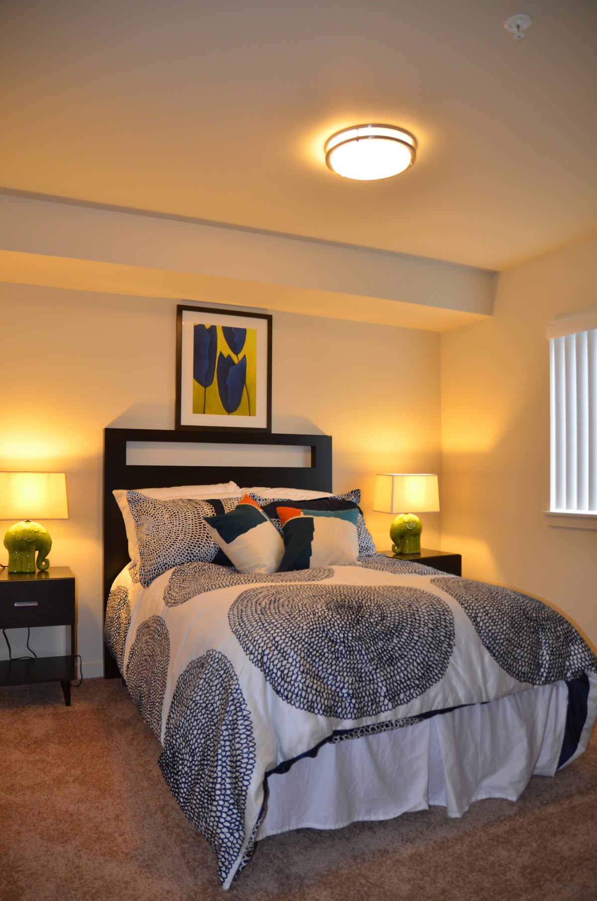 A modern bedroom with stylish decor, featuring a neatly made bed, two lamps on nightstands, and artwork above the headboard.