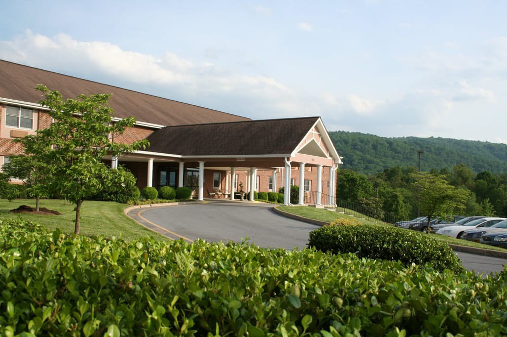 A scenic view of a building surrounded by lush greenery and hills under a clear sky.
