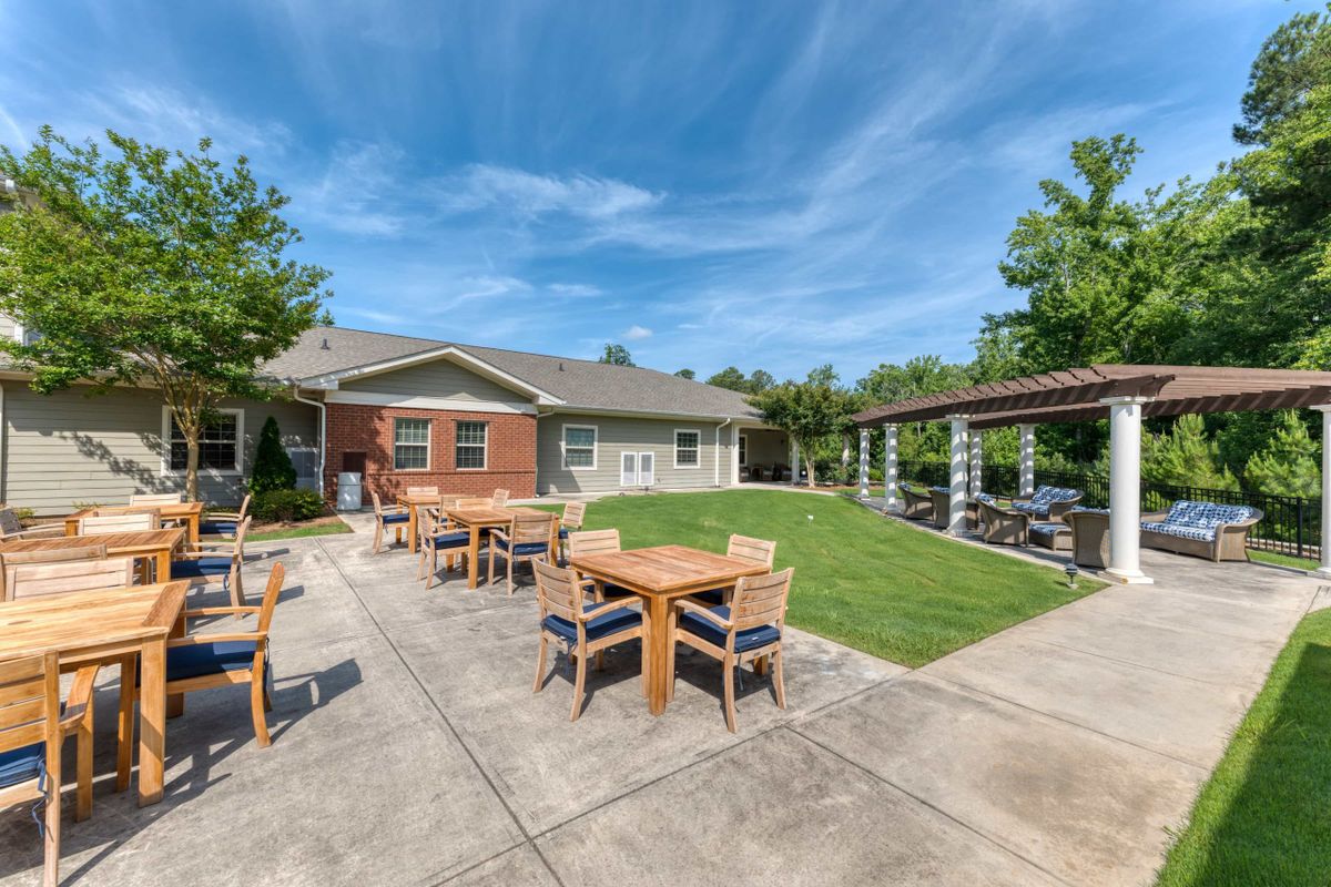 A sunny patio area with tables and chairs, adjacent to a house and lawn.