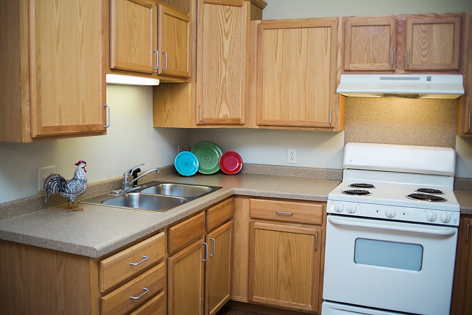 A compact kitchen with wooden cabinets, a stove, and a double sink.