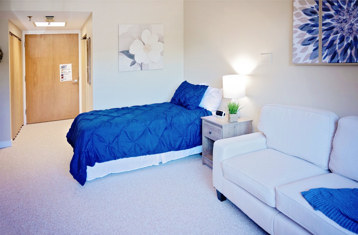 A minimalist bedroom with a blue bedspread, white furniture, and soft lighting.