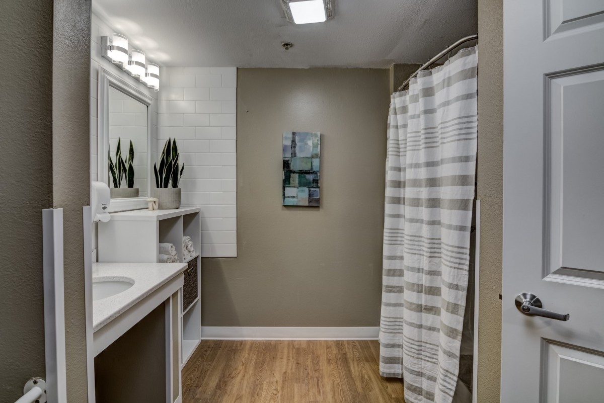 A modern bathroom featuring a sink with a mirror, decorated with plants, and a shower enclosed by a striped curtain.