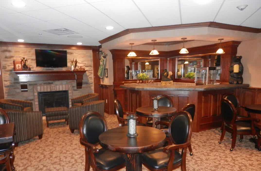 A cozy bar interior with wooden decor, featuring tables, chairs, and a fireplace.