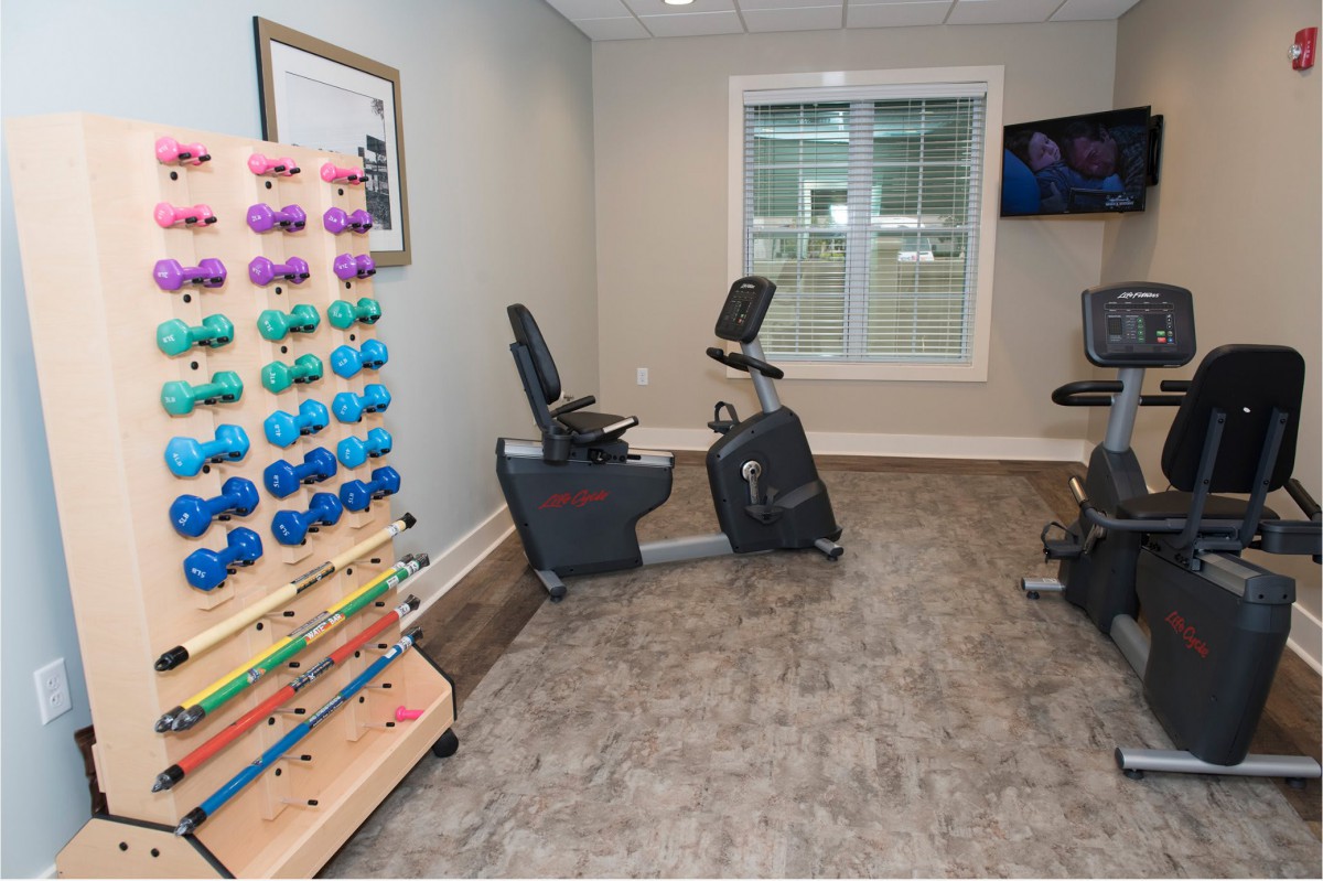A home gym featuring two stationary bikes and a rack of colorful dumbbells.