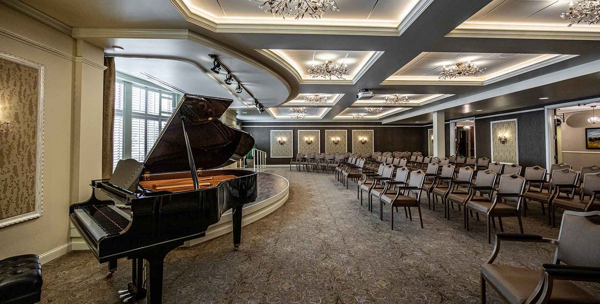 An elegant concert hall interior featuring a grand piano on stage and arranged seating.