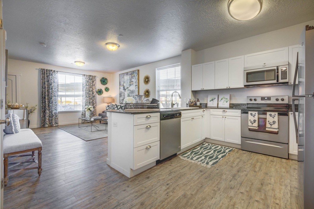 A modern kitchen with an open floor plan connecting to a cozy living area, featuring white cabinets and hardwood flooring.