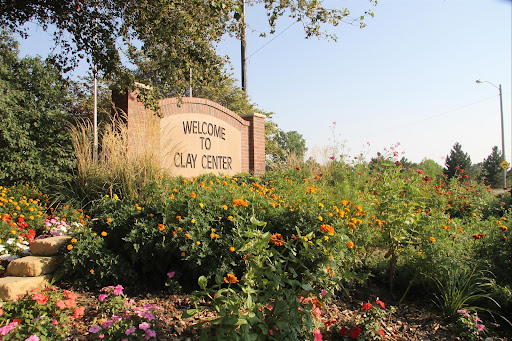 A welcoming sign to Clay Center, surrounded by vibrant flowers and lush greenery.
