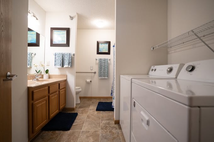 A spacious bathroom with a laundry area, featuring a washing machine, double sink vanity, and neatly arranged towels.