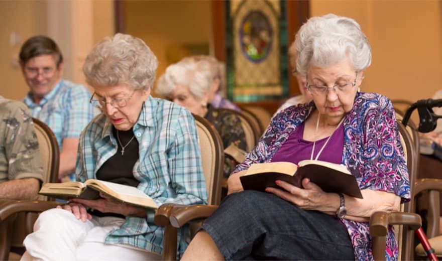 A group of elderly women are sitting indoors, engaging in reading books together.
