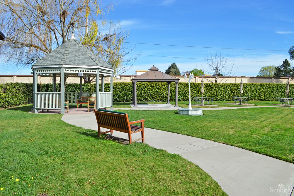 A peaceful park scene with a gazebo, bench, and paved pathway on a sunny day.