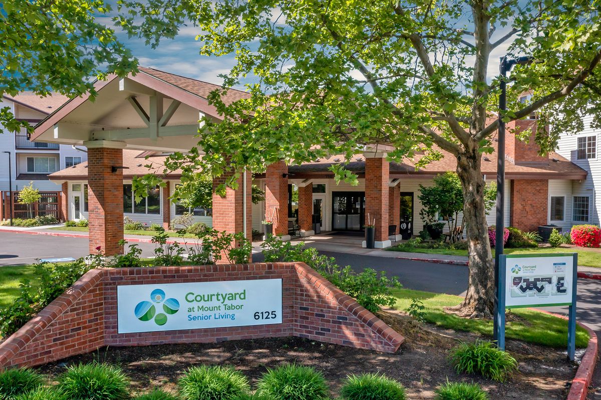 Entrance of a building with signage and surrounding trees and landscaping.