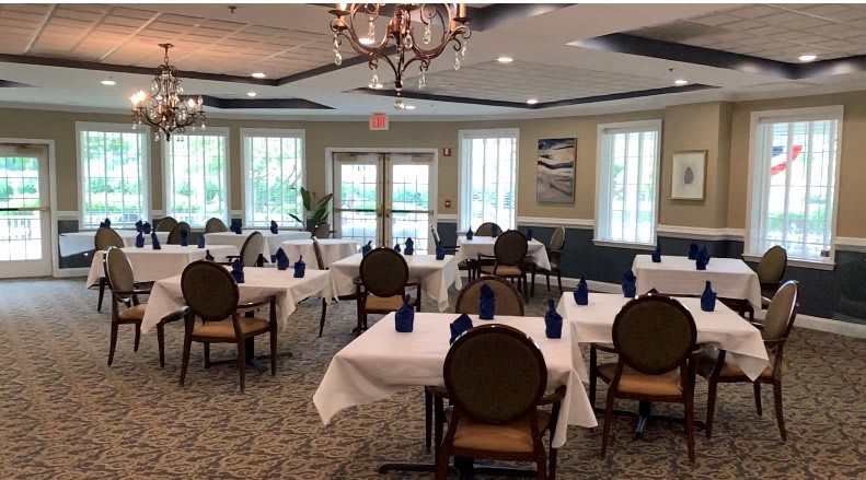 An elegant dining room with neatly arranged tables and chairs, featuring white tablecloths and a chandelier.