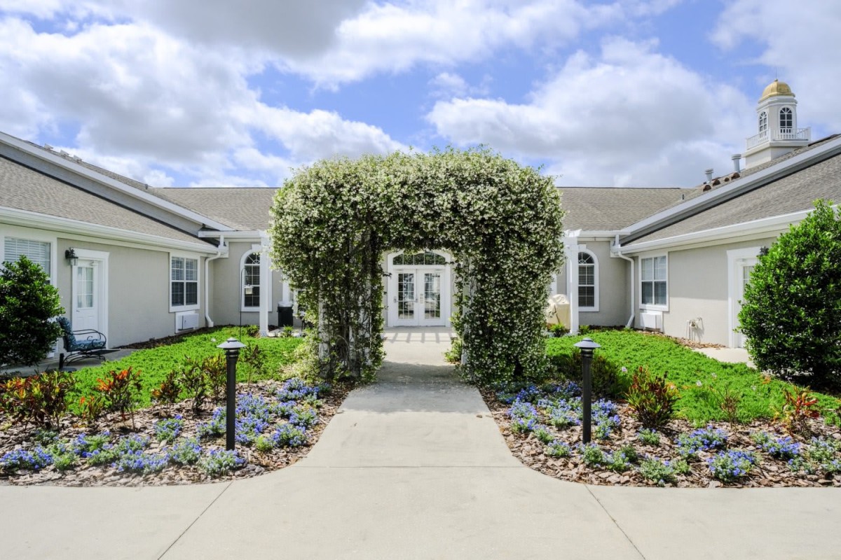 A beautifully landscaped garden with a flowering archway leading to a building.