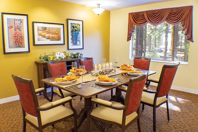 A warmly lit dining room with a decorated table set for a meal, surrounded by upholstered chairs and adorned with framed artwork on the yellow walls.