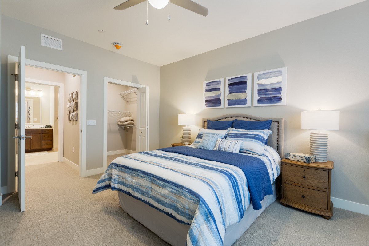 A modern bedroom with a blue and white color scheme featuring a neatly made bed, bedside tables, and wall art.