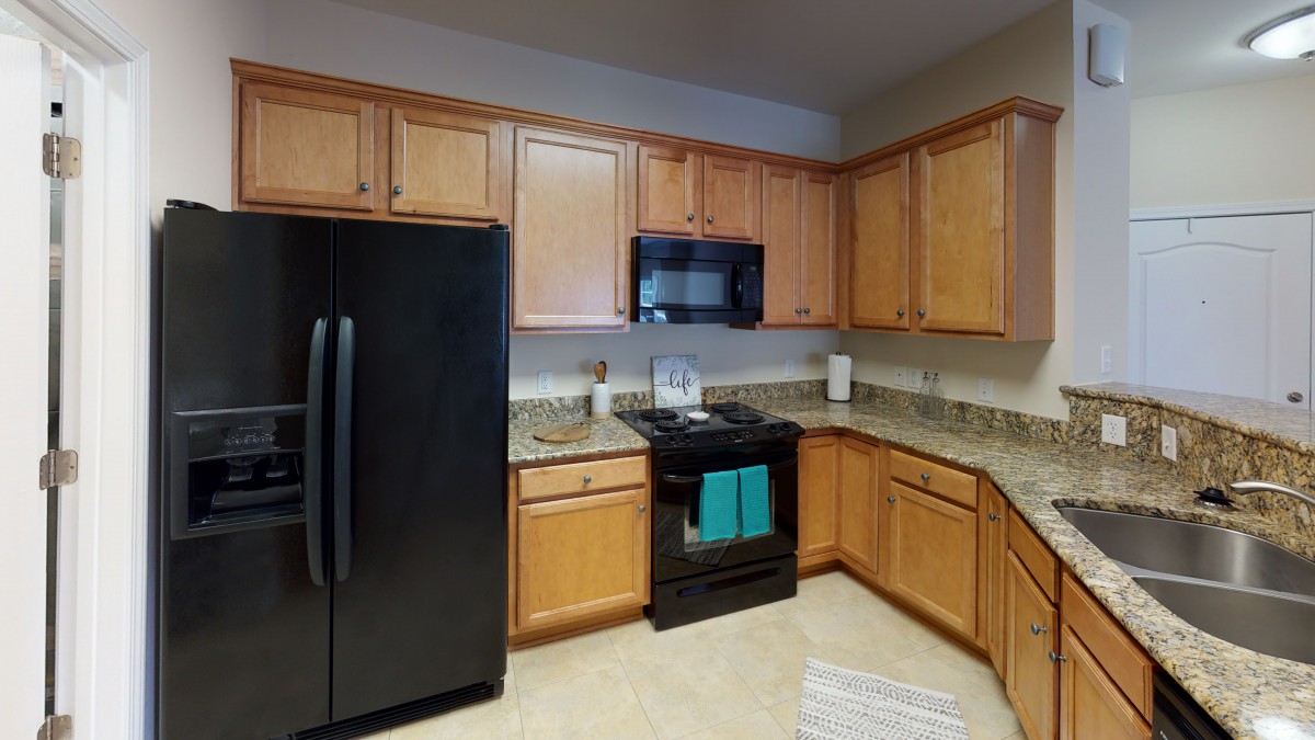 A modern kitchen with wooden cabinets, black appliances, and tiled flooring.