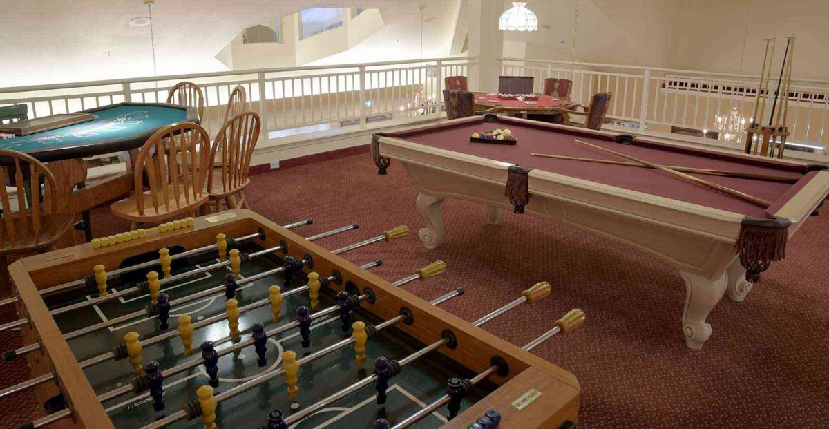 An indoor game room featuring a foosball and pool table, complete with wooden furniture and carpeted flooring.
