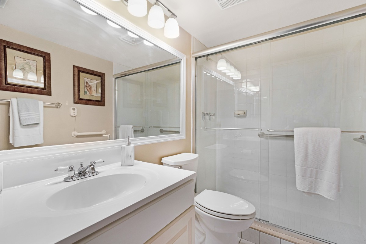 A clean and modern bathroom with a large mirror, sink, toilet, and shower.