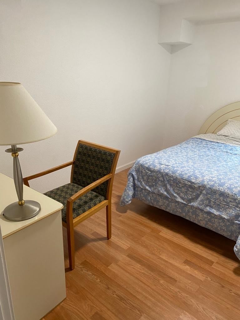 A minimalist bedroom featuring a bed, chair, lamp, and wooden flooring.