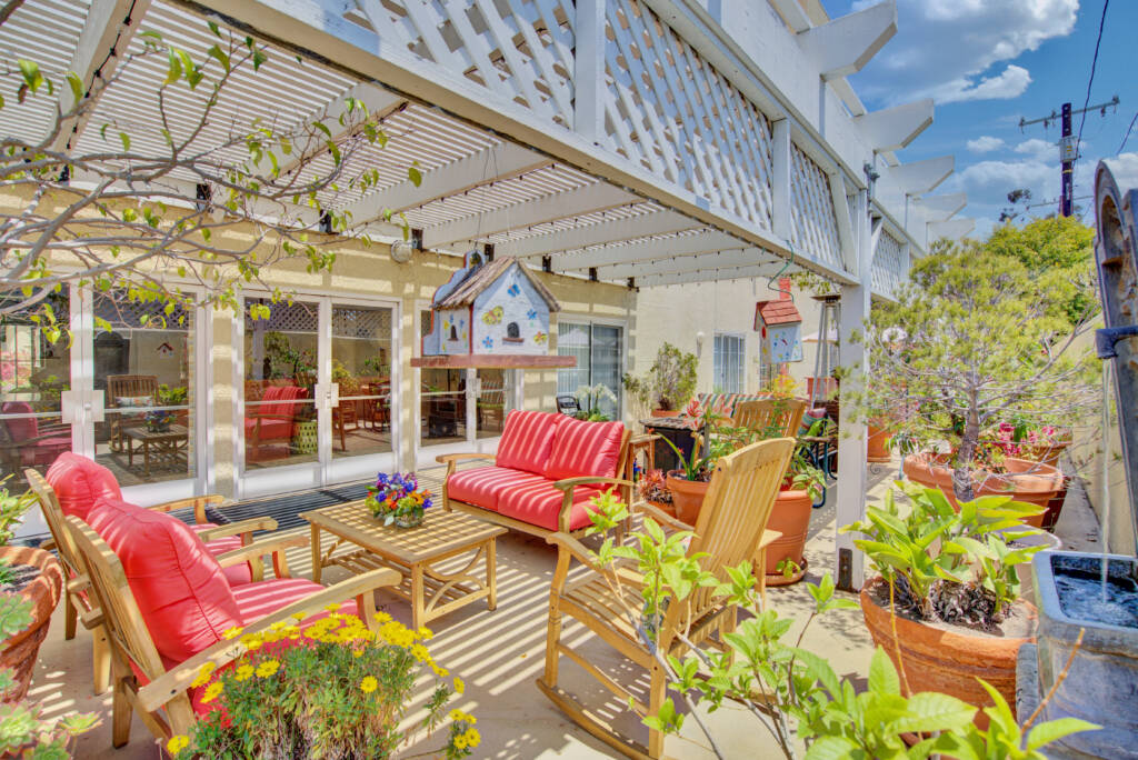 A vibrant outdoor patio area featuring comfortable seating and lush greenery under a pergola.