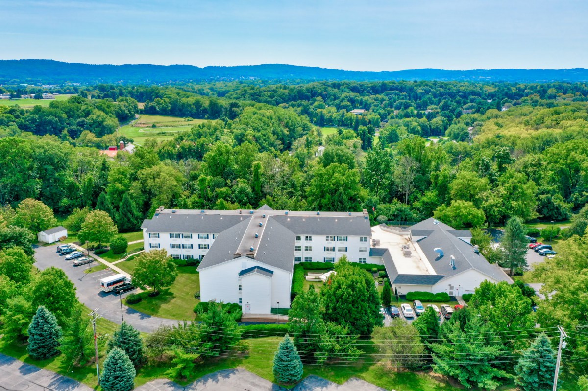 Aerial view of a large building nestled in lush greenery and rolling hills.