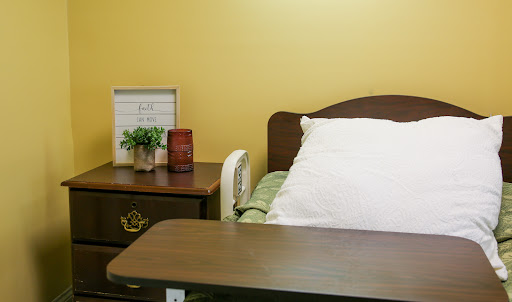 A cozy hospital room featuring a bed, nightstand with plants, and a simple decor.