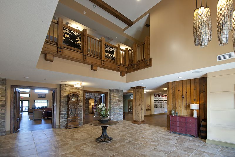 A spacious hotel lobby featuring wooden accents, stone pillars, and a balcony.