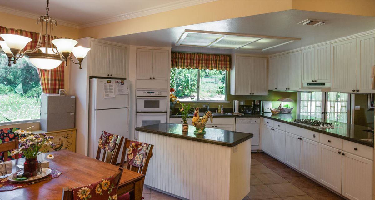 A modern kitchen with an island countertop, dining area, and large window letting in natural light.