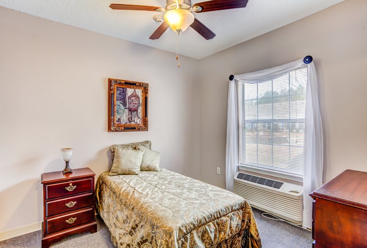 A cozy bedroom with a single bed, ceiling fan, and large window.