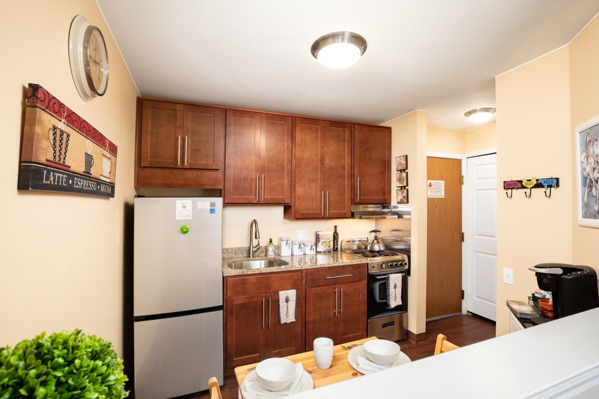 A modern apartment kitchen with wooden cabinets and a compact dining area.