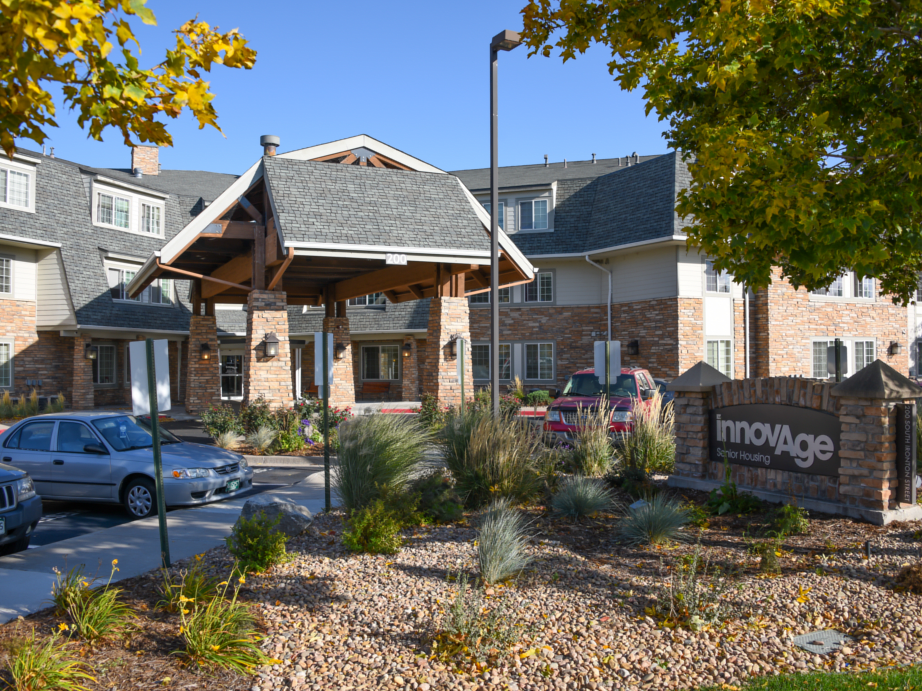 An exterior view of a senior living facility entrance surrounded by landscaped greenery.