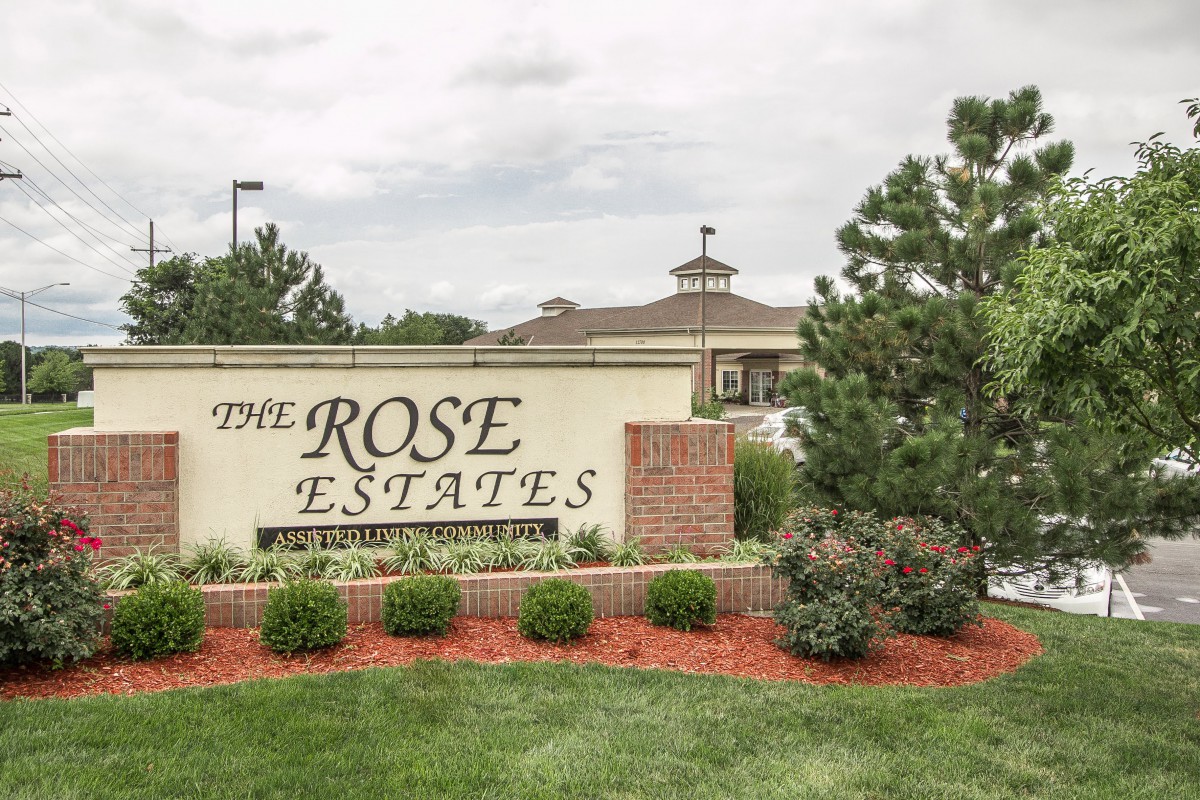 Entrance sign for The Rose Estates surrounded by landscaping.
