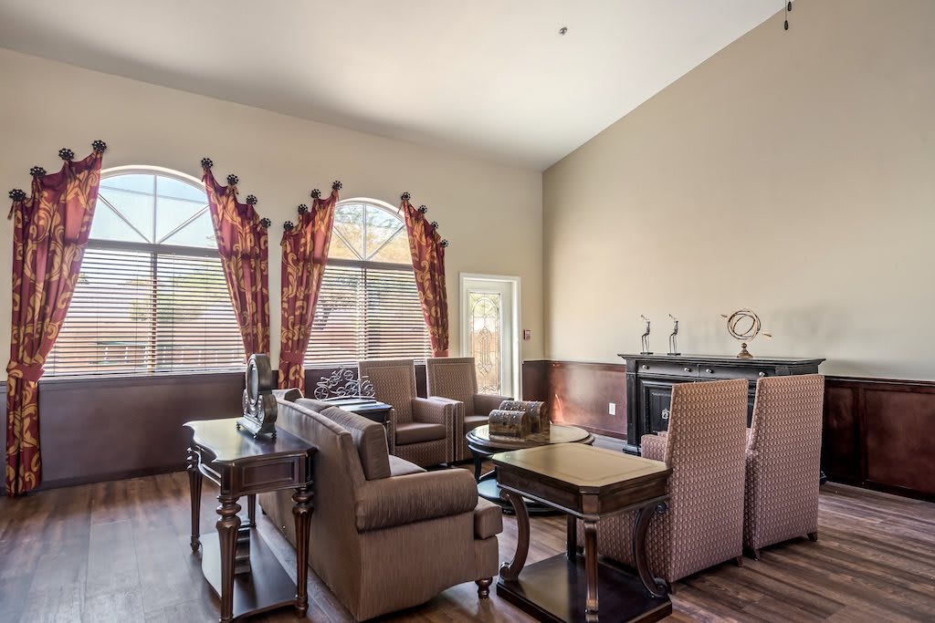 A cozy living room with high ceilings, featuring comfortable seating, a fireplace, and large windows with decorative curtains.